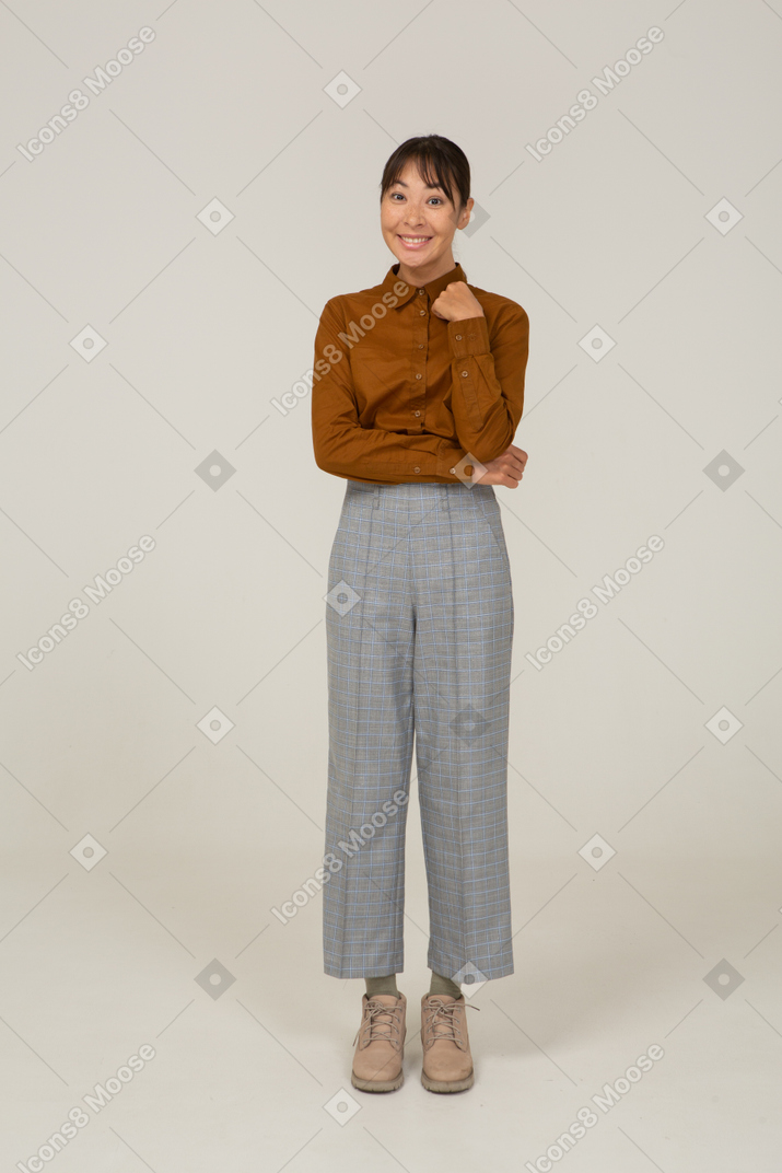 Front view of a smiling young asian female in breeches and blouse touching neck