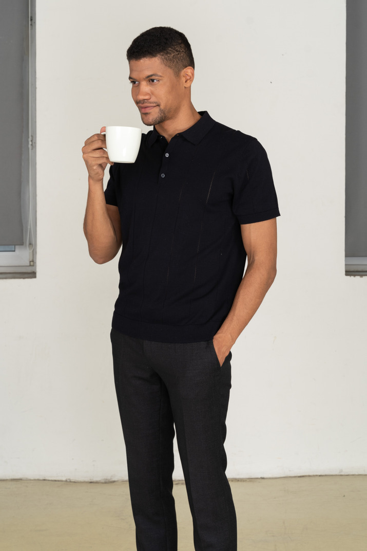 Standing half sideways young man in black pants and t-shirt holding cup