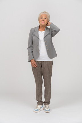 一位身着西装的老妇人手放在头后站着的前视图