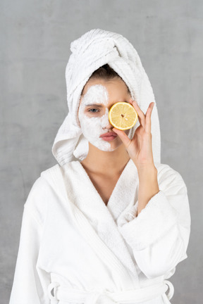 Portrait of a woman in bathrobe pouting and holding a lemon over eye