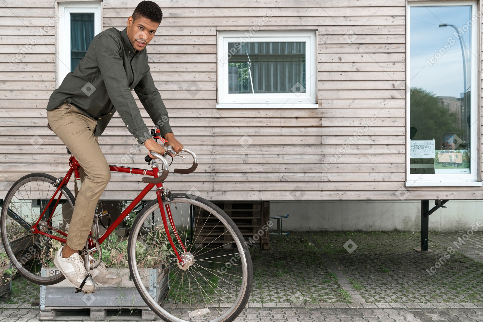 A man riding a red bike next to a house