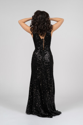 Woman in black evening dress standing back to camera and holding head