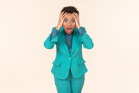 Black woman with a short haircut, wearing all blue, standing against a plain pastel background, looking emotional