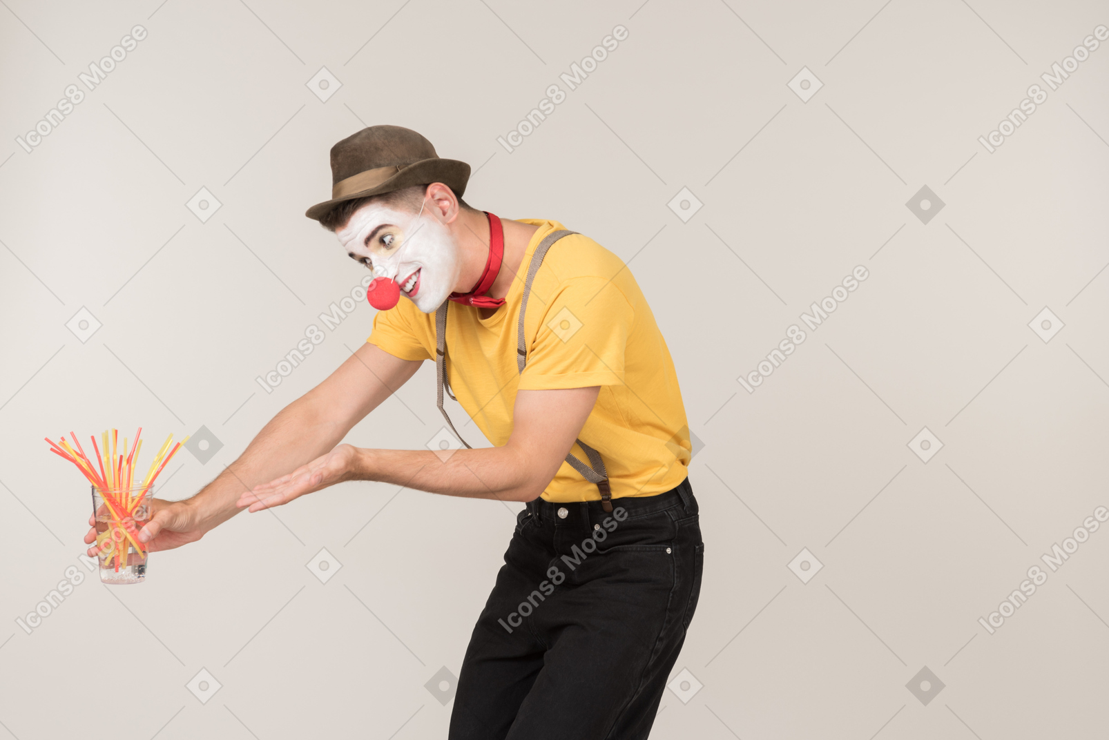 Sad male clown pointing at glass of plastic straws he's holding