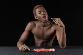 Vista frontal de un joven afro comiendo carne cruda