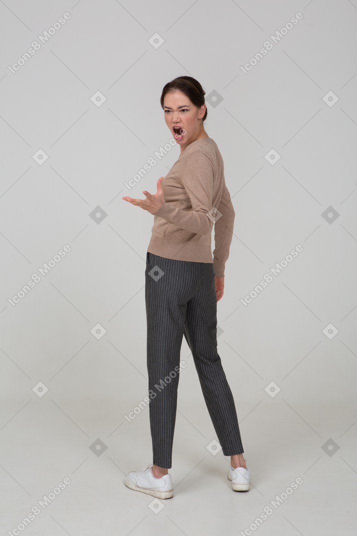Three-quarter back view of a furious gesticulating young lady in beige pullover