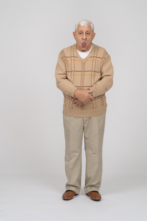 Front view of an old man in casual clothes showing tongue