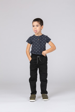 Front view of a cute boy posing with hand in pocket and showing tongue