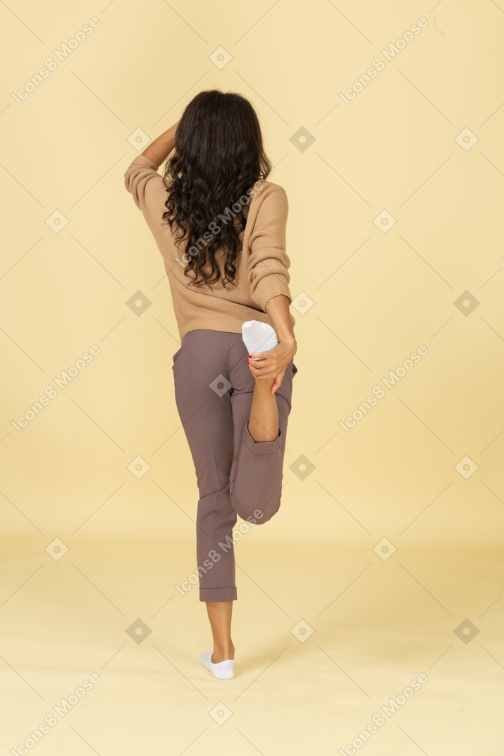 Vista traseira de uma jovem mulher de pele escura tocando sua perna e tornozelo