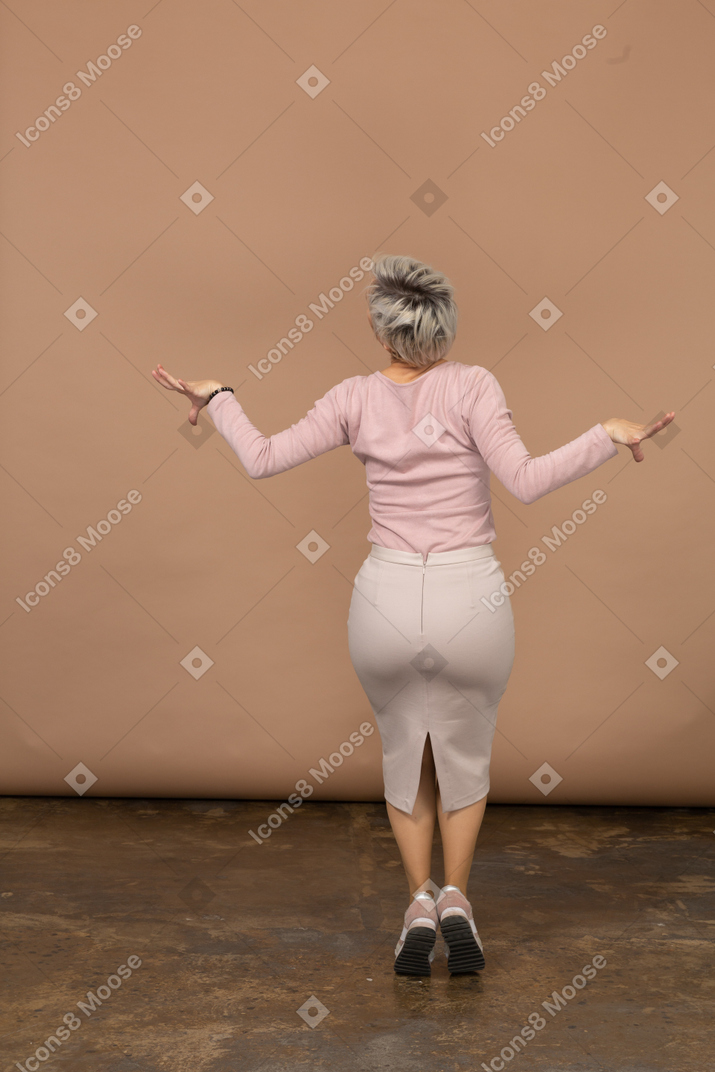 Вид сзади женщины в повседневной одежде прыгает и разводит руками