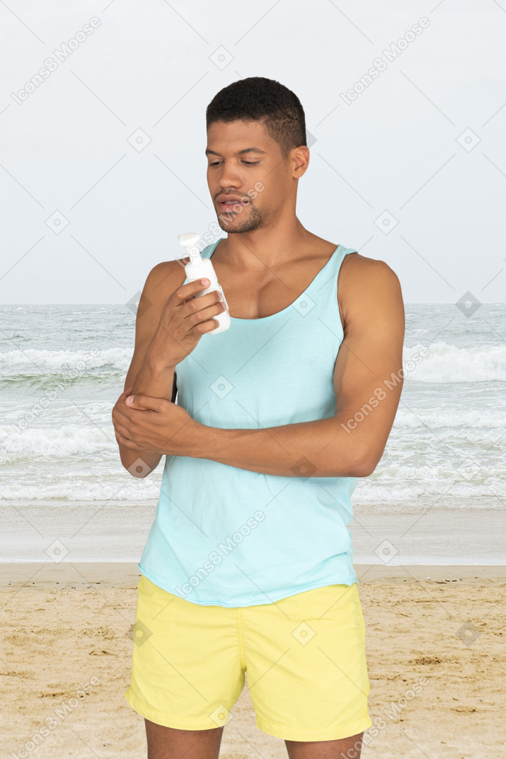 A man standing on a beach holding a bottle of sunscreen