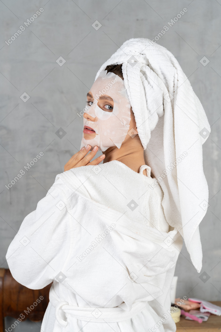 Back view of a woman in bathrobe with a face mask on turning her head