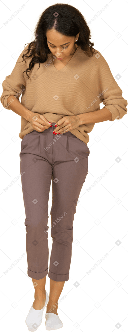 Vue de face d'une jeune femme à la peau sombre zipper son pantalon