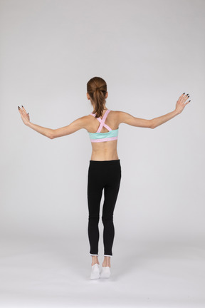 Back view of a teen girl in sportswear balancing on tiptoes while raising hands