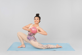 Молодая индийская гимнастка растягивает себя сидя на коврик для йоги и держа мяч