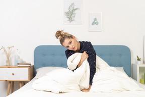 Front view of a tired young woman in pajamas with blanket staying in bed