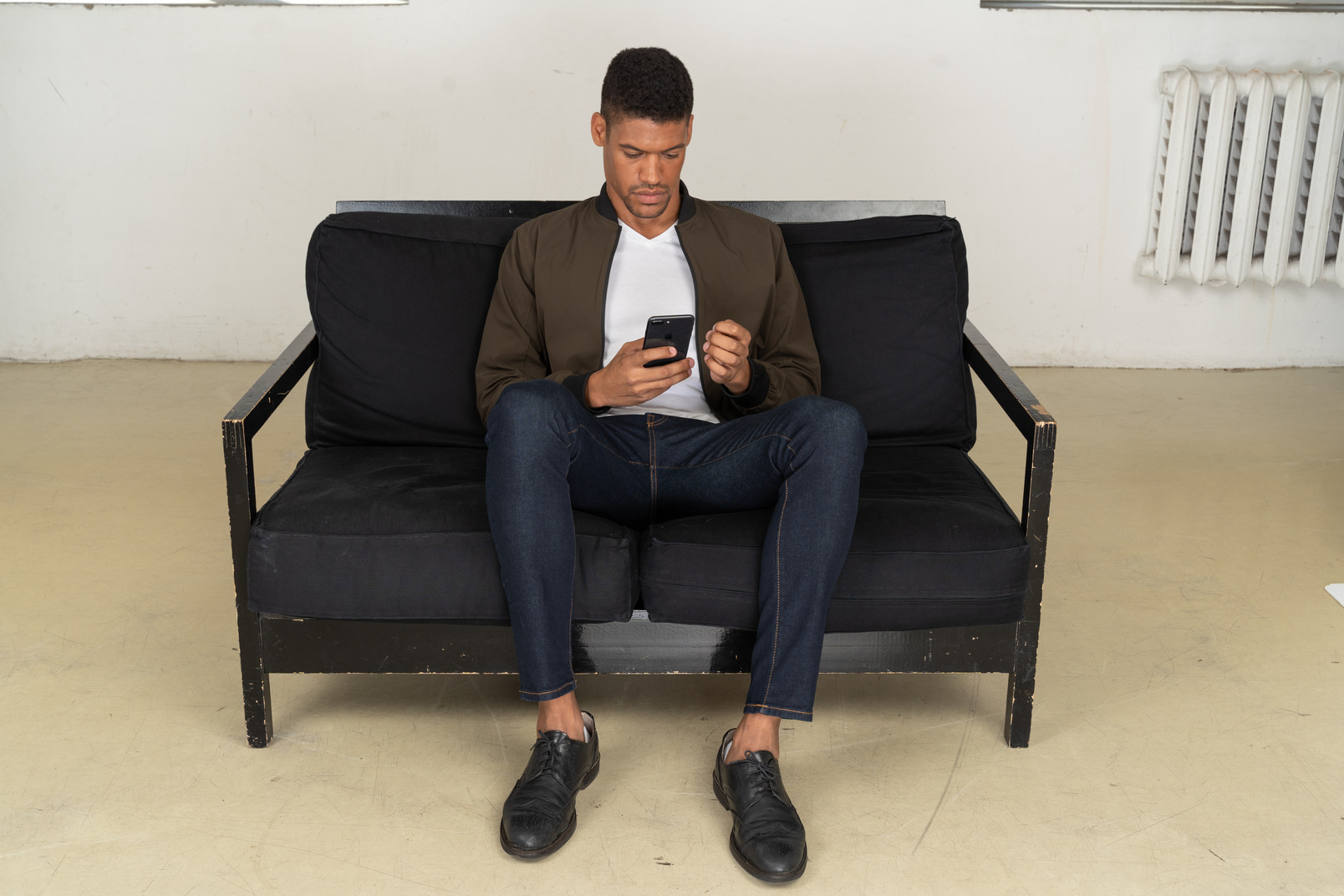 Front view of a young man sitting on a sofa and watching his phone
