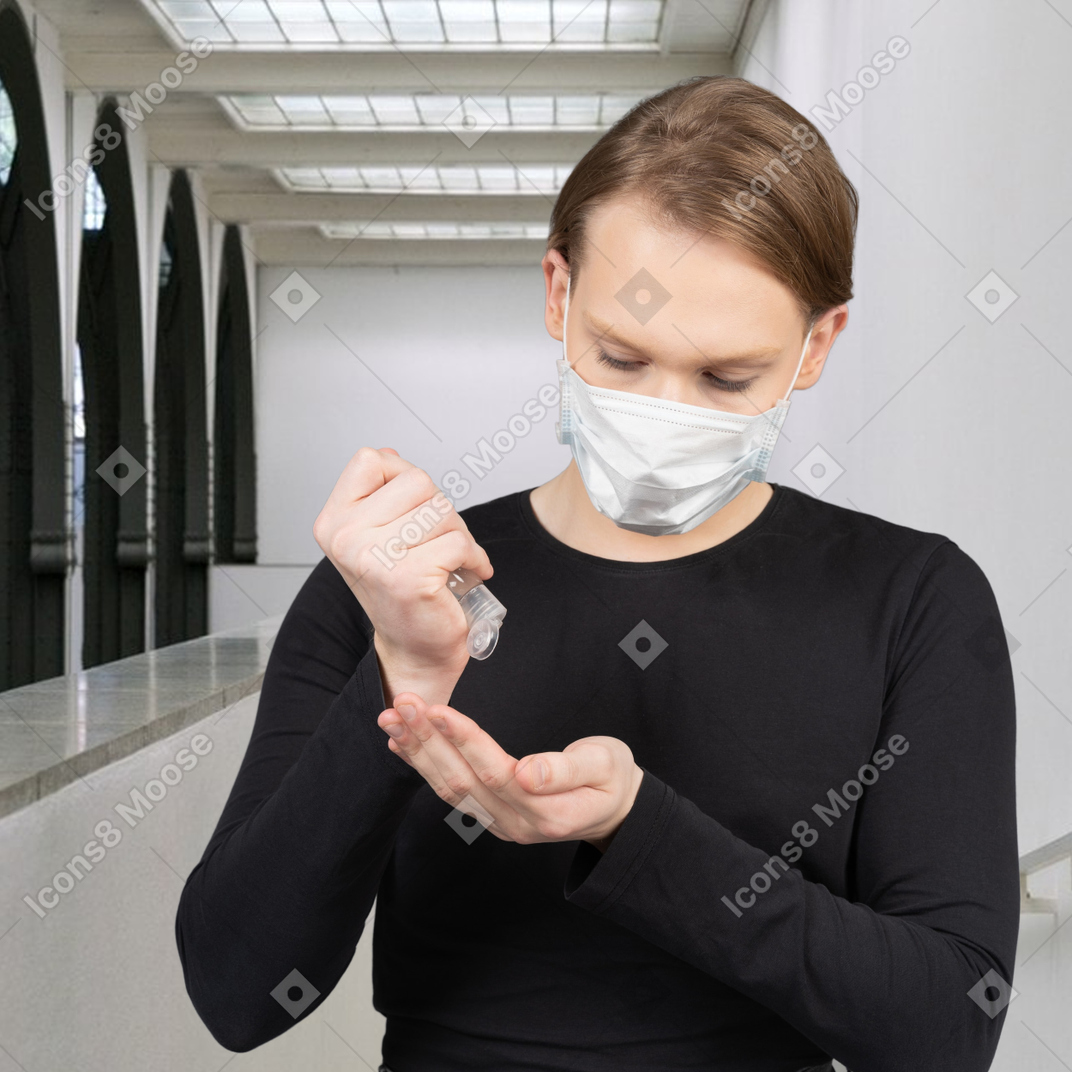 A young man in a mask using a hand sanitizer