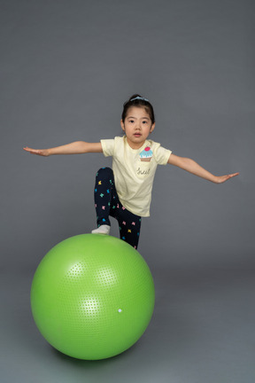 Bambina che calpesta un fitball verde con le braccia aperte