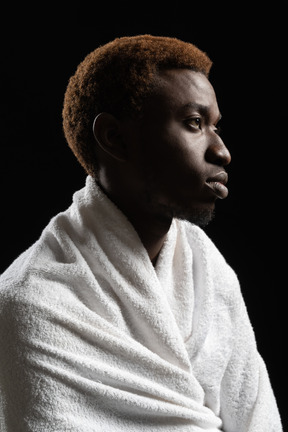 Боковой снимок молодого мужчины, сидящего, завернутого в полотенце