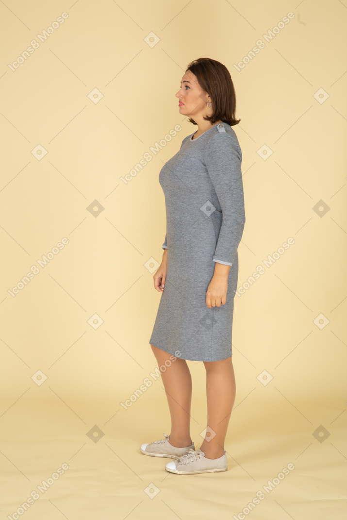 Женщина в сером платье стоит в профиль