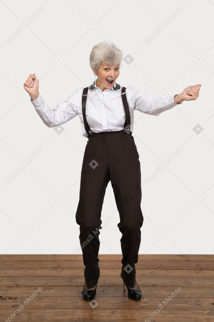 Front view of a happy old lady in office clothing raising hands while screaming