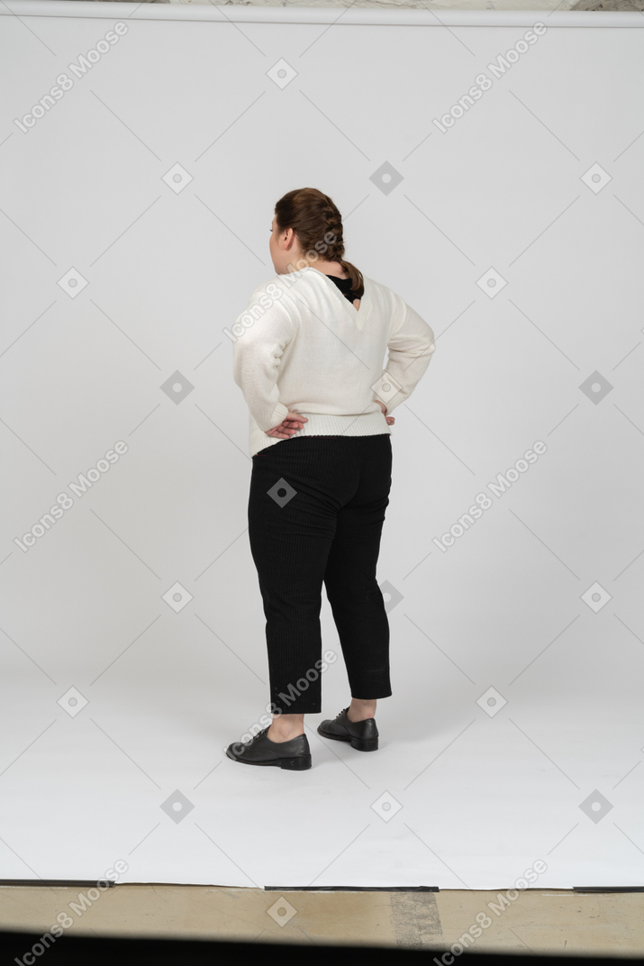 Вид сзади пухлой женщины в повседневной одежде, стоящей с руками на бедрах