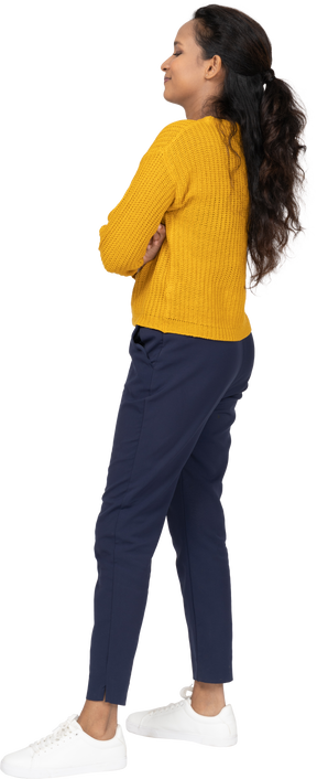 Vista lateral de una niña feliz en ropa casual posando con los brazos cruzados
