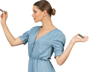 Vista di tre quarti di una giovane donna in abito blu con in mano un rossetto