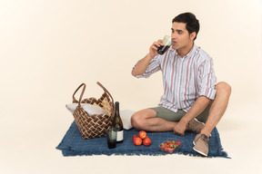 Jovem homem caucasiano sentado no cobertor e bebendo vinho