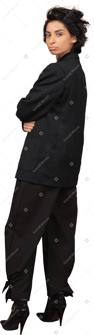 Vue de trois quarts d'une femme d'affaires coquine dans un costume noir faisant la moue et regardant la caméra