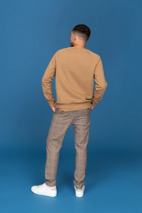 Young man with hands in pockets standing back to camera