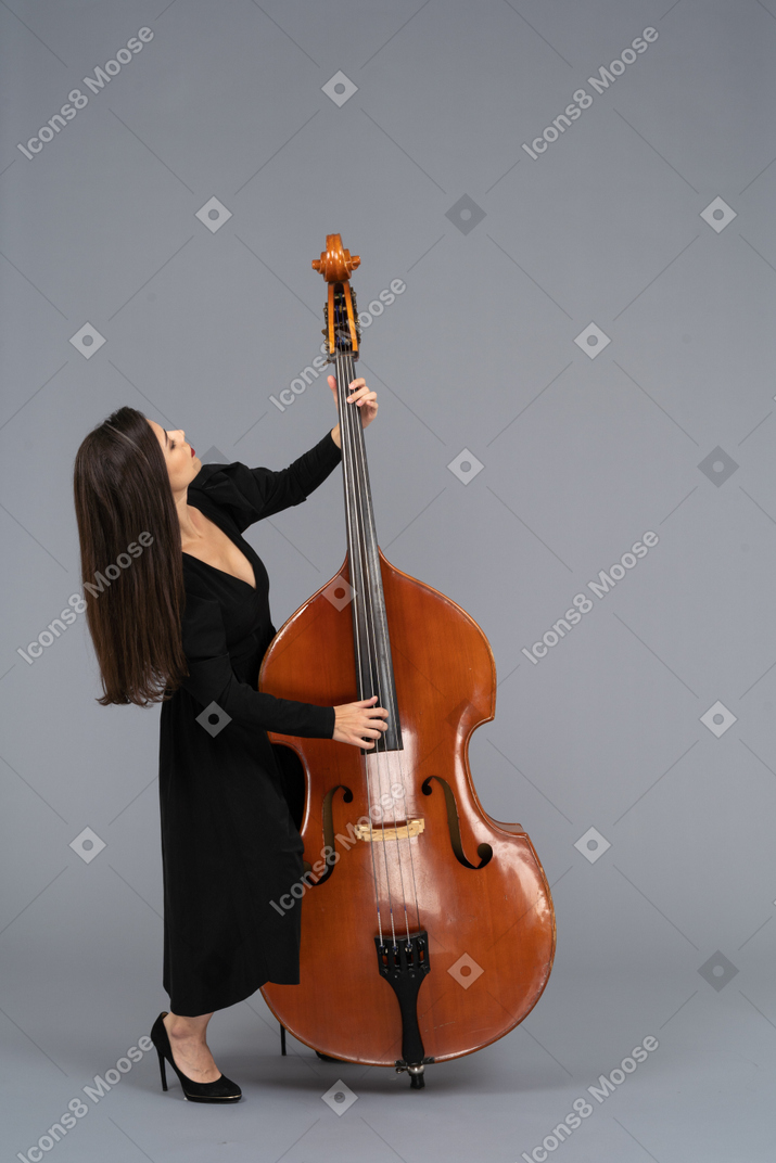 Молодая женщина в черном платье в полный рост, играющая на контрабасе, откинувшись назад