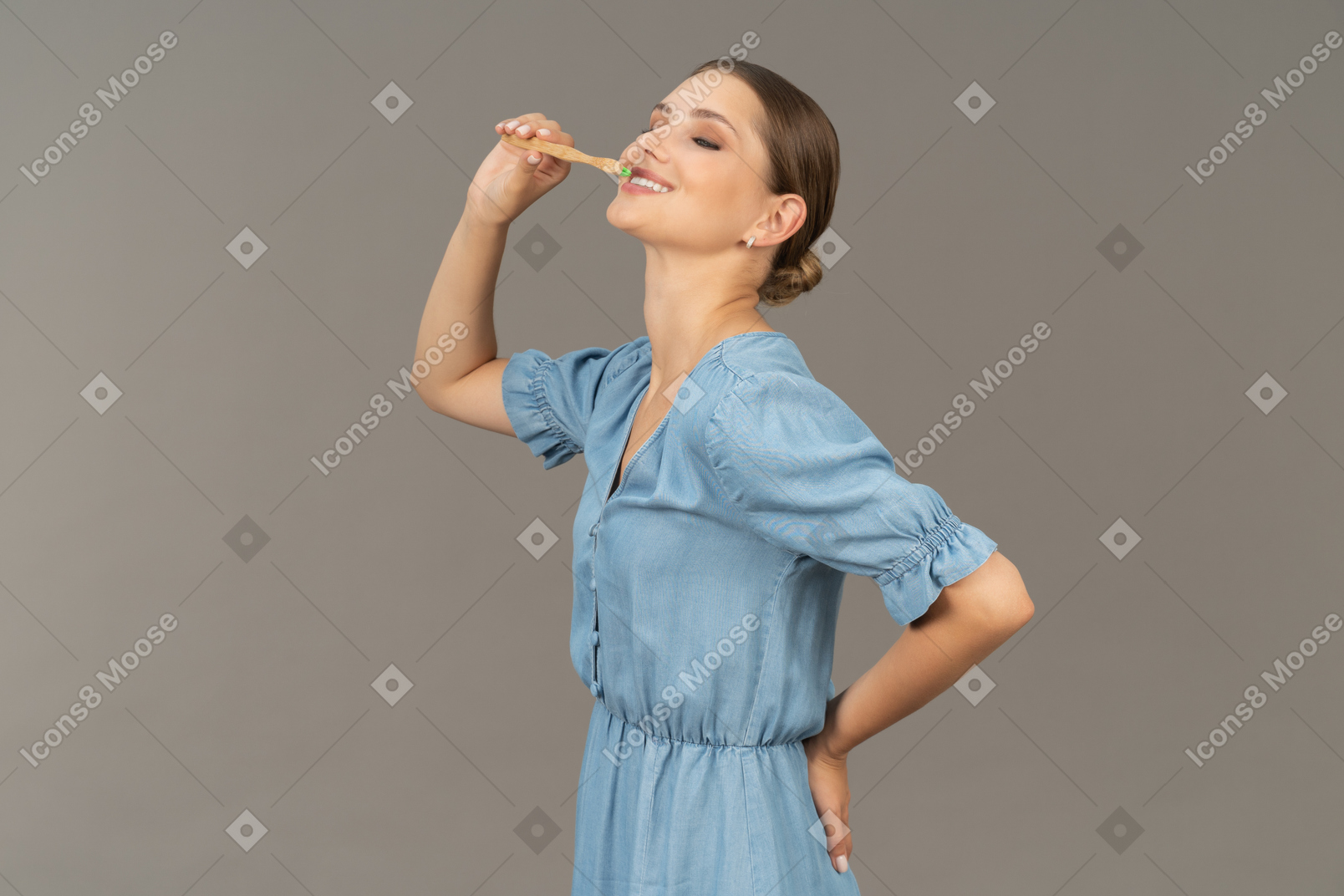 Three-quarter view of a young woman in blue dress brushing her teeth