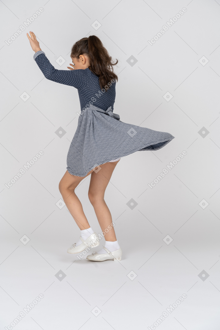 Vista trasera de tres cuartos de una niña bailando con las manos en el aire