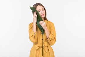 Young woman closing her face with green leaf with eyes closed