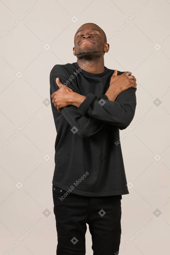 Pleased black man embracing himself with closed eyes
