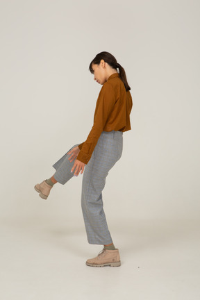 Vista posteriore di tre quarti di una giovane donna asiatica in calzoni e camicetta che alza la gamba