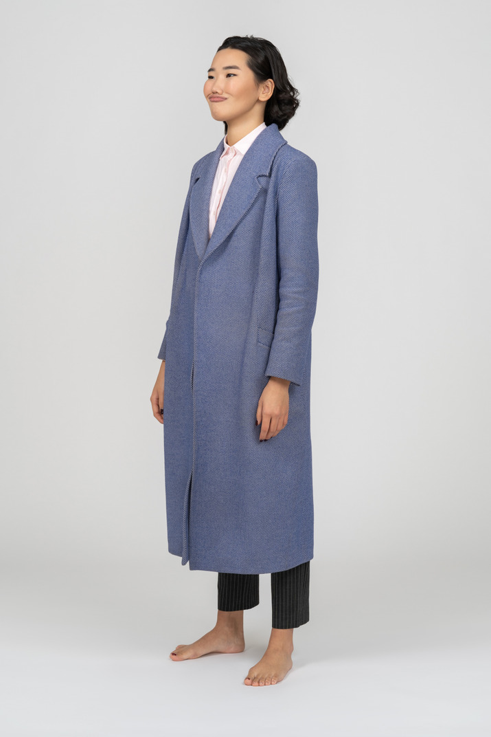 Young woman in long blue coat with dislike facial expression standing half sideways
