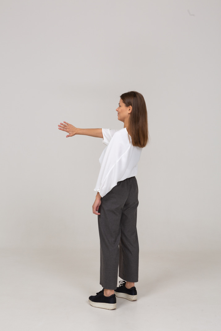 Three-quarter back view of a displeased young lady in office clothing outstretching arm