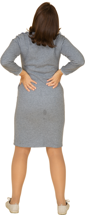 Vista posteriore di una donna in abito grigio che soffre di dolore nella parte bassa della schiena
