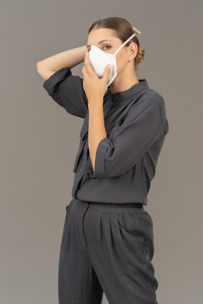 Woman in gray coveralls putting on a respirator