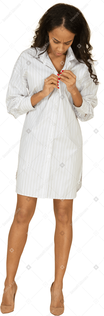 Vista frontal de una mujer joven de piel oscura abotonándose su vestido blanco