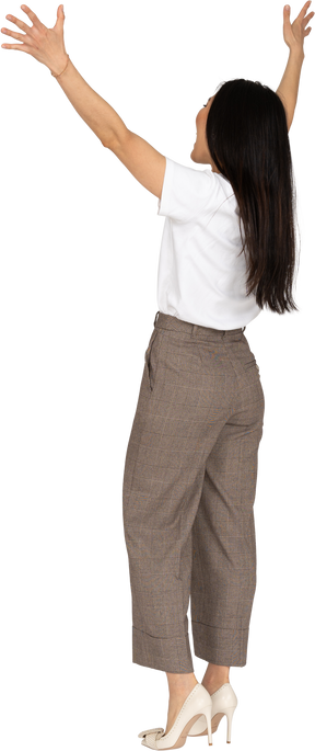 Three-quarter back view of a happy young lady in breeches and t-shirt raising hands