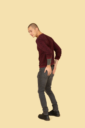 Three-quarter view of a young man in red pullover touching his back pockets