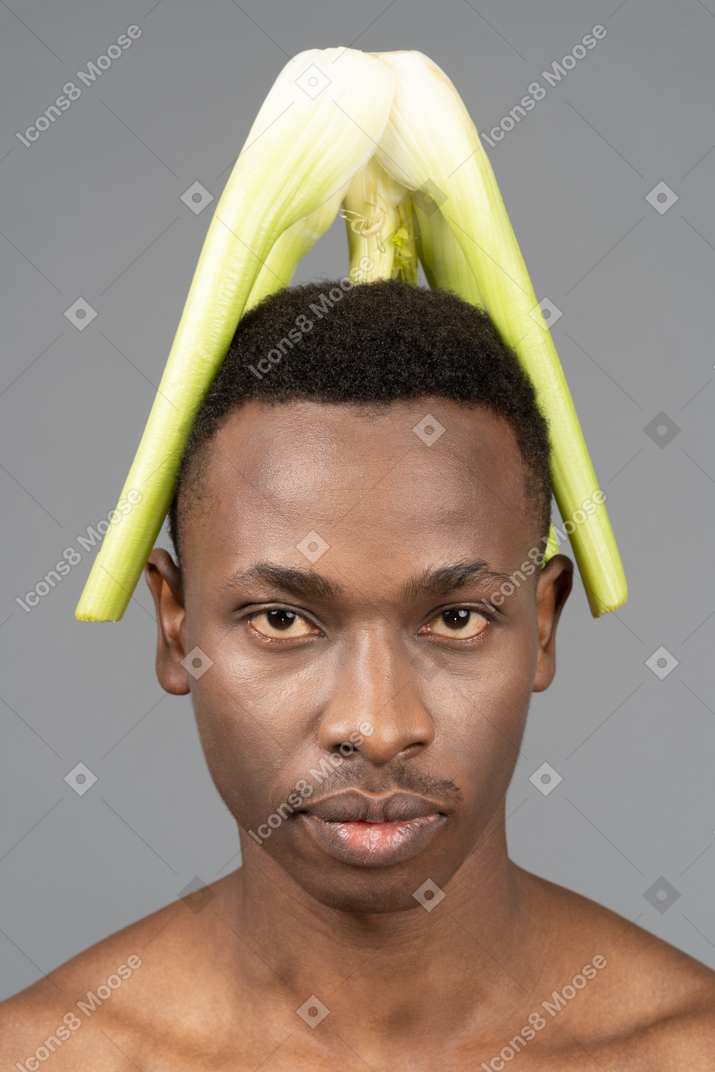 A shirtless young man with a celery on his head