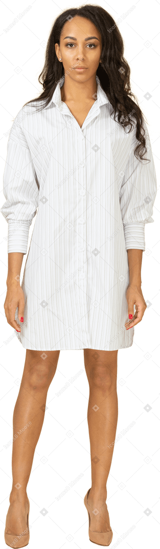 Vista frontal de uma jovem mulher de pele escura confiante em um vestido branco olhando para a câmera