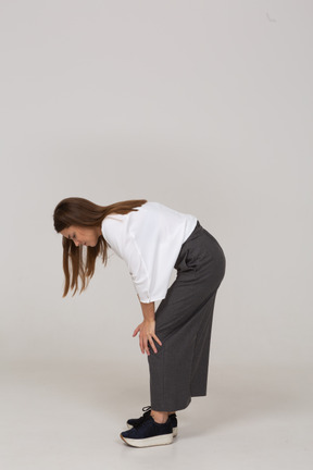一位身着办公室服装的年轻女士弯下腰触摸膝盖的侧视图