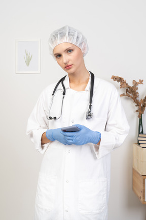 Front view of a young female doctor with stethoscope holding her phone