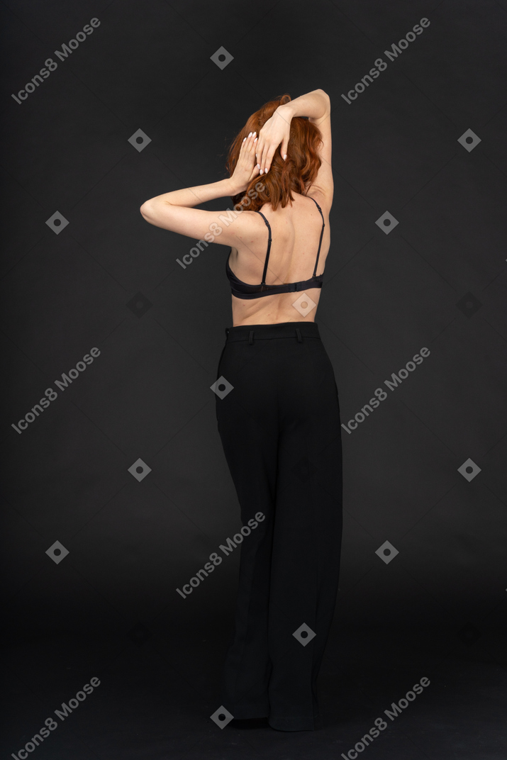 A back side view of the young sexy woman on the black background touching her hair